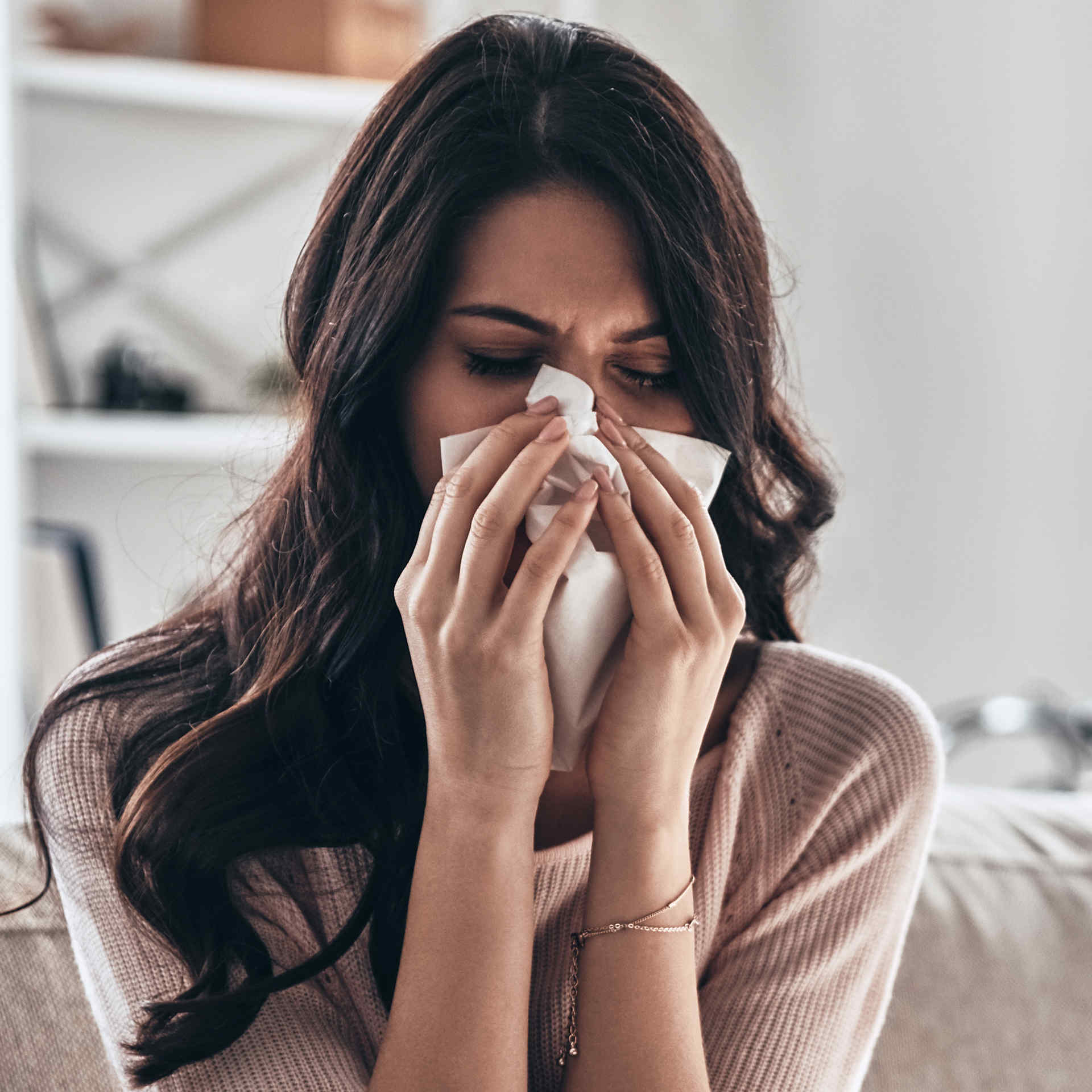 A sick South Asian woman sitting with a napkin close to her nose from allergy.
