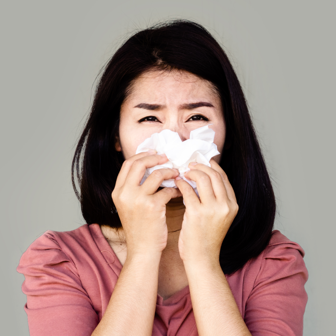 一位亚洲妇女因过敏而用餐巾纸紧贴鼻子。