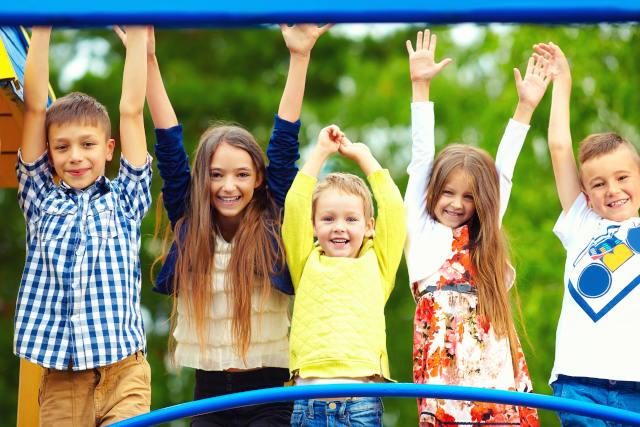 Five kids happily raising their hands in an outdoor playground